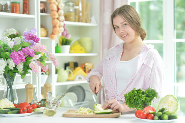 Cute teen girl preparing fresh salad on kitchen table   - Foto, afbeelding
