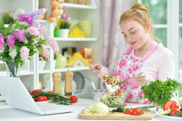 Cute teen girl preparing fresh salad on kitchen table   - Foto, immagini
