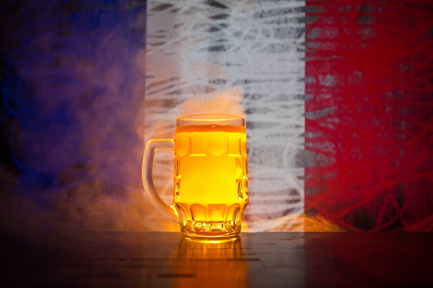 Koncepcja kreatywnych. Kufel świeże piwo na stole z niewyraźne banderą Francji na tle lub szklankę piwa lager gotowy do picia. Kopiować miejsca. Selektywny fokus - Zdjęcie, obraz