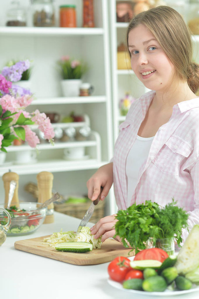 Cute teen girl preparing fresh salad on kitchen table   - Fotografie, Obrázek