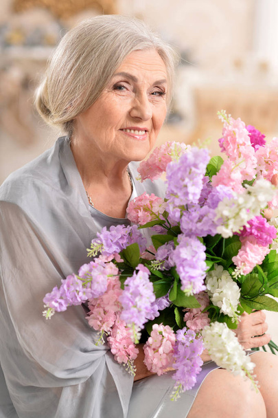 Close up portrait of beautiful senior woman posing at home with flowers  - Foto, Bild