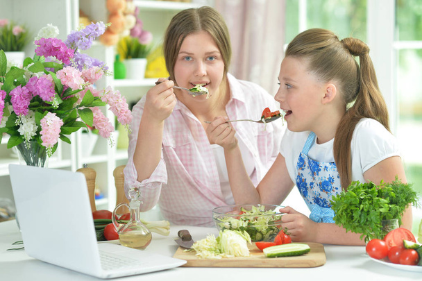 Two funny girls preparing fresh salad on kitchen table   - Foto, afbeelding