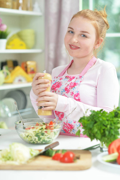 Cute teen girl preparing fresh salad on kitchen table   - Foto, Bild