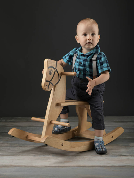 Sweet little boy playing at home with wooden horse, childhood games - Photo, Image
