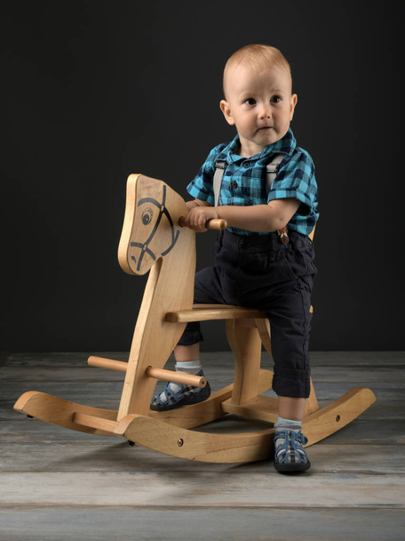 Милый мальчик играет дома с деревянной лошадью, детские игры
 - Фото, изображение