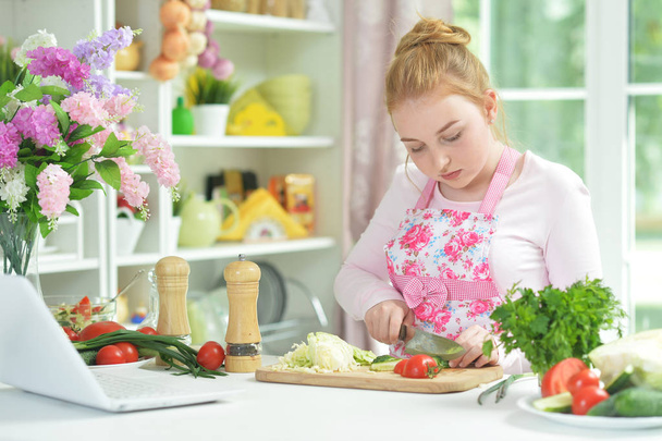 Cute teen girl preparing fresh salad on kitchen table   - Foto, afbeelding