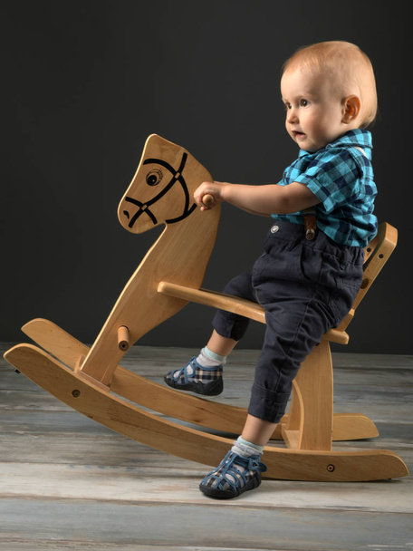 Sweet little boy playing at home with wooden horse, childhood games - Фото, изображение