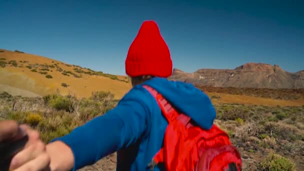 Sígueme - mujer joven feliz en sombrero rojo con mochila tirando de los chicos de la mano. Mano a mano a pie lanzan el Parque Nacional del Teide, Tenerife, Islas Canarias, España
. - Metraje, vídeo
