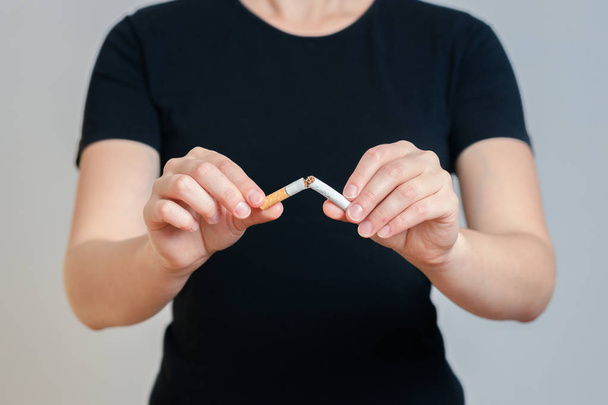 Девушка в черной одежде разбивает сигарету. на сером фоне. Концепция запрета курения
 - Фото, изображение