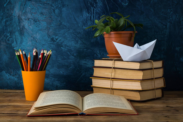 Open Book, A Pile of Books, A Paper Boat, Colored Pencils on a Darkly Blue Background. - Foto, Bild