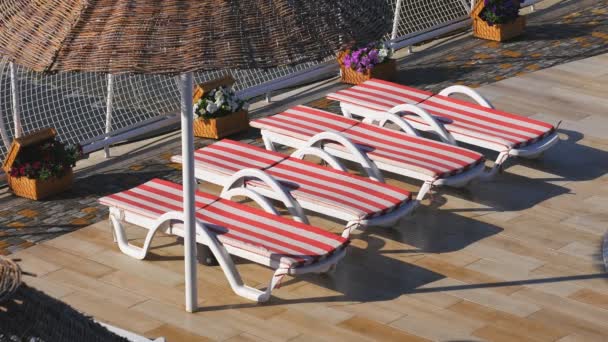 Hotellin ja rannan lähellä on tyhjät aurinkotuolit. Aamulla rannalla, rannalla aurinkotuoleja ja aurinkovarjoja
. - Materiaali, video
