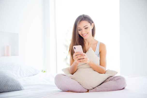 Portrait of pretty charming girl sitting on bed chatting with friends holding smart phone using wifi 3G internet - Фото, зображення