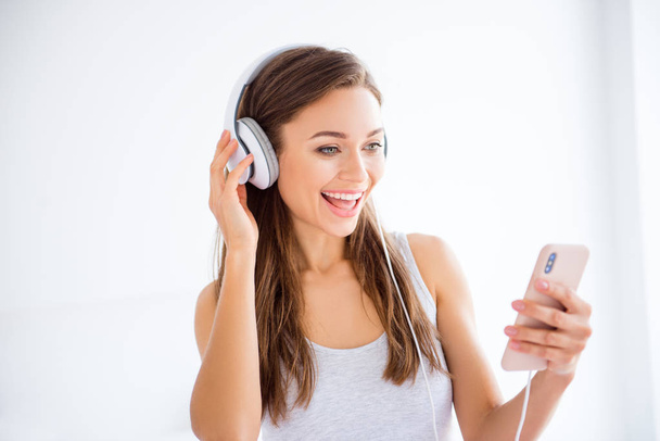 Head shot portrait of cheerful positive girl using smart phone and headset listening favorite music enjoying free time - Фото, изображение