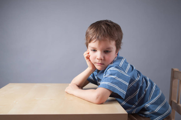 Portrait of little boy. child is sitting at table, gray background - Photo, Image