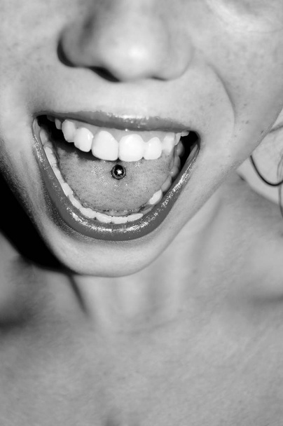 schöne Frau streckt ihre Zunge heraus und zeigt ihre junge piercing schwarz-weiß - Foto, Bild