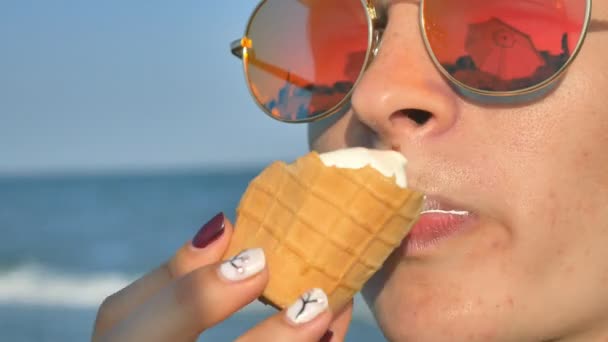 Joven morena lamiendo comiendo helado en la playa, fondo azul marino y gafas de sol
. - Metraje, vídeo
