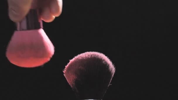 Make-up brushes with pink powder on a black background in slow motion - Metraje, vídeo