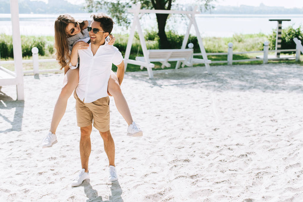 smiling boyfriend giving piggyback to girlfriend at city beach - Foto, Bild