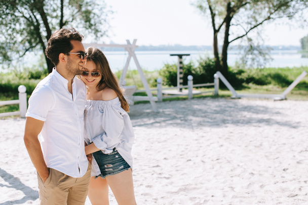 happy couple in casual clothes and sunglasses standing on sandy city beach - Foto, Imagem