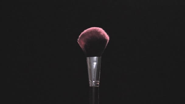 Make-up brushes with pink powder on a black background in slow motion - Felvétel, videó