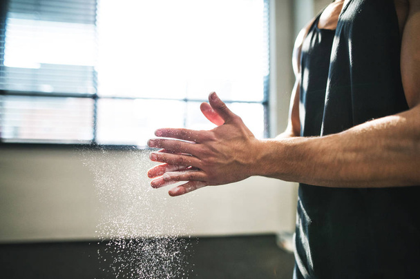 Ein fitter junger Mann im Fitnessstudio schmiert seine Hände mit Magnesium. Nahaufnahme. - Foto, Bild
