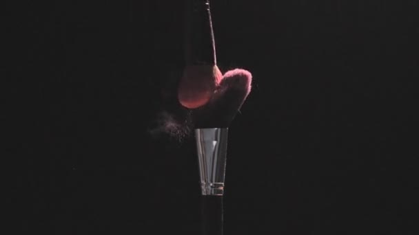 Make-up brushes with pink powder on a black background in slow motion - Filmagem, Vídeo