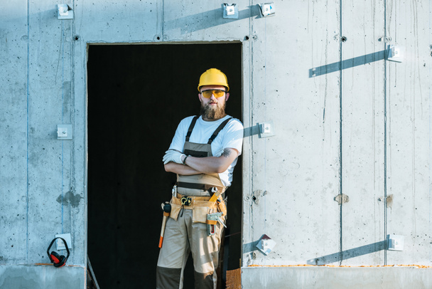  rakentaja suojaava googles ja kypärä seisoo ristissä aseiden rakennustyömaalla
  - Valokuva, kuva