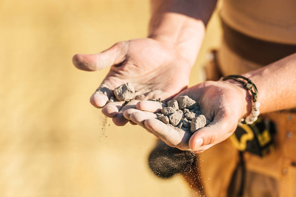 περικομμένη εικόνα εργάτης οικοδομών, κρατώντας στο χέρι πέτρες παλάμες  - Φωτογραφία, εικόνα