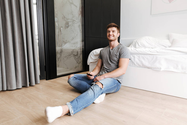 Happy young man sitting with tv remote at his bedroom - Valokuva, kuva