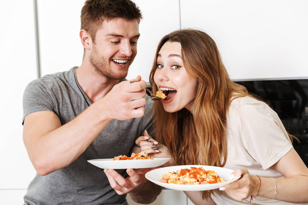 Cheerful young couple feeding each other with breakfast in a kitchen - Foto, immagini