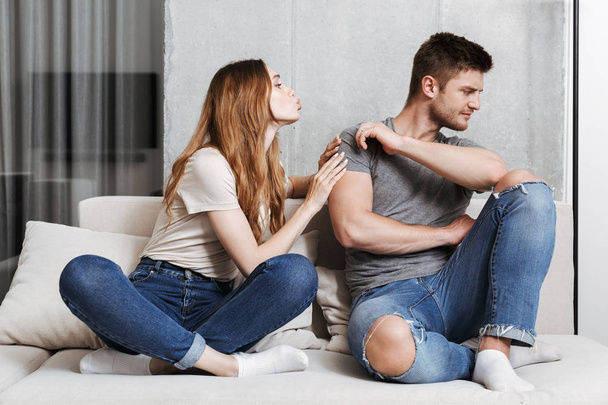 Pretty young woman trying to kiss her boyfriend while sitting together on a couch at home - Foto, immagini