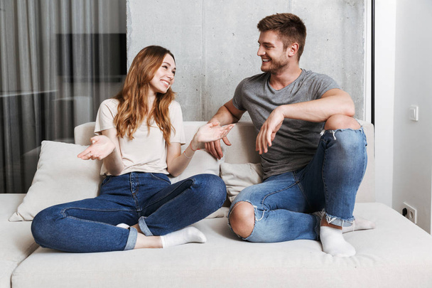Happy couple talking while sitting together on a couch at home - Φωτογραφία, εικόνα