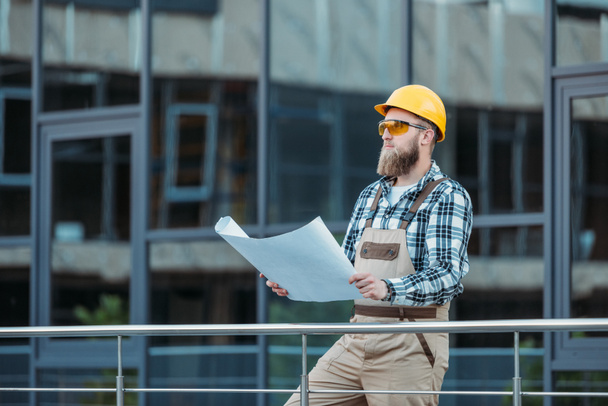 young construction worker in protective googles and hardhat looking at blueprint   - Photo, Image