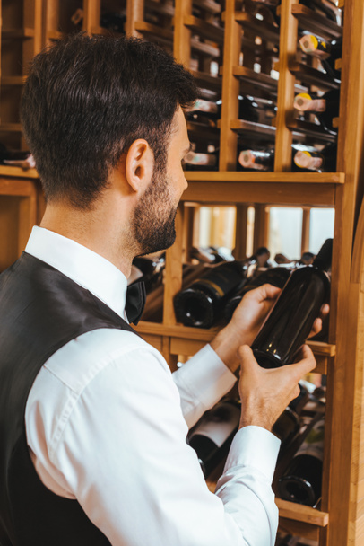 apuesto joven sommelier tomando botella de estante en tienda de vinos
 - Foto, imagen