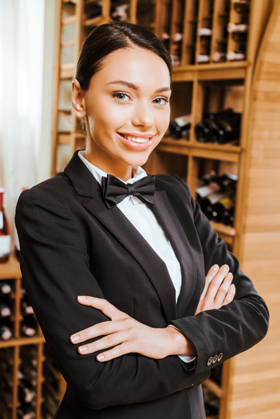 sorridente mordomo do vinho feminino com braços cruzados olhando para a câmera na loja de vinhos
 - Foto, Imagem