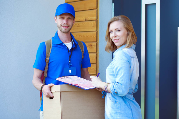 Smiling delivery man in blue uniform delivering parcel box to recipient - courier service concept. Smiling delivery man in blue uniform - Φωτογραφία, εικόνα