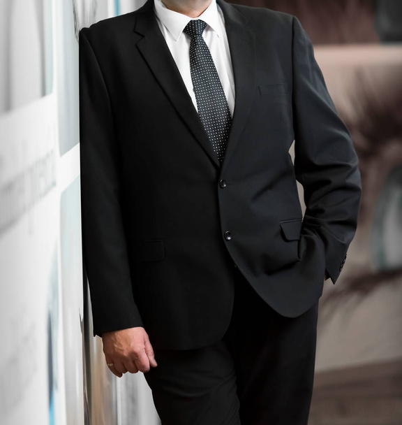 Περικοπεί κεφάλι άνθρωπος στέκεται σε ένα έξυπνο κοστούμι με το χέρι, ένα χέρι στην τσέπη σε ένα γραφείο - Φωτογραφία, εικόνα