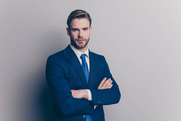 Portrait with copy space of cool, brutal, stunning, brunet, serious, concentrated man with stubble in blue suit with tie, having his arms crossed, looking at camera, isolated on grey background - 写真・画像