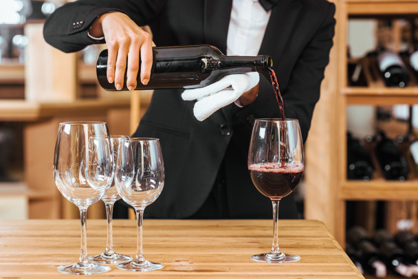 cropped shot of female wine steward pouring wine into glasses at wine store - 写真・画像