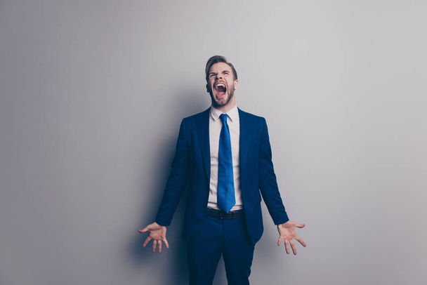 Fail! Portrait of violent, stylish, attractive, angry man in blue suit, tie with bristle, hairstyle, yelling loud with wide open mouth, gesture palms, isolated on grey background - Foto, immagini