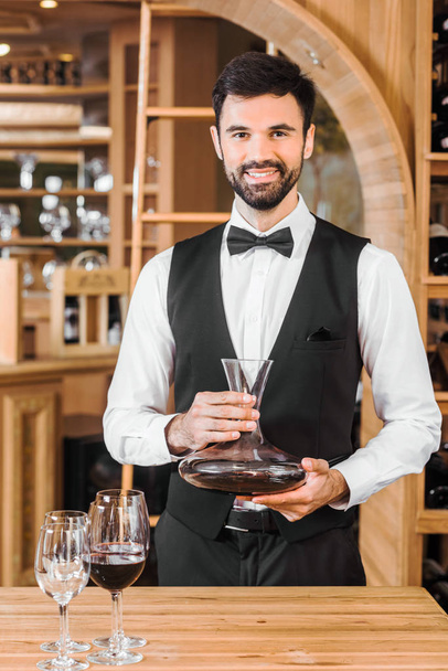 handsome young sommelier holding decanter of red wine at wine store - Photo, Image