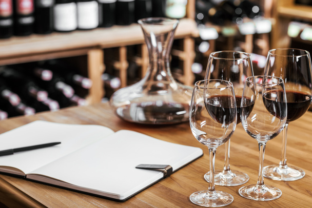 close-up shot of decanter of red wine with notebook and glasses on wooden table at wine storage - Photo, Image
