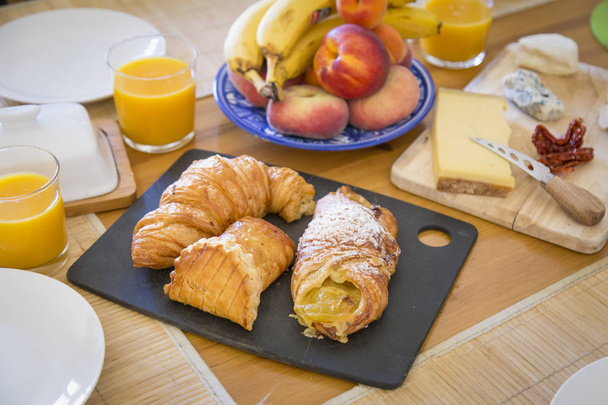 Здоровый вкусный завтрак стол с сыром, поджаренный хлеб, круассаны, кондитерские изделия, апельсин и манго
 - Фото, изображение