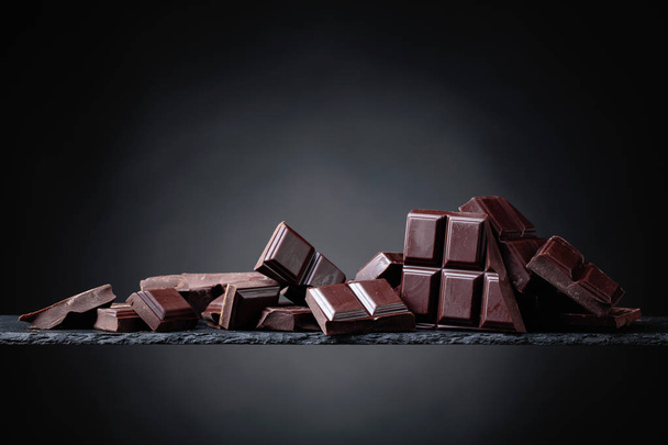 Broken chocolate pieces on a black background. Copy space. - Photo, Image