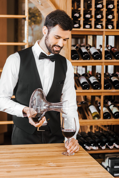 handsome young sommelier pouring wine from decanter at wine store - Fotó, kép
