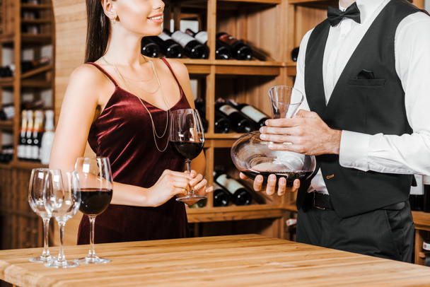 tiro recortado de mayordomo de vino celebración decantador de vino en frente de cliente femenino en la tienda de vinos
 - Foto, Imagen