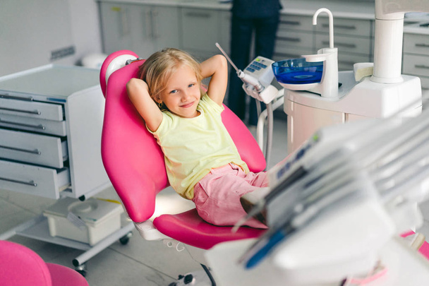 歯科医のオフィスで椅子に座ってしばらくの間カメラを見て笑顔の子供 - 写真・画像