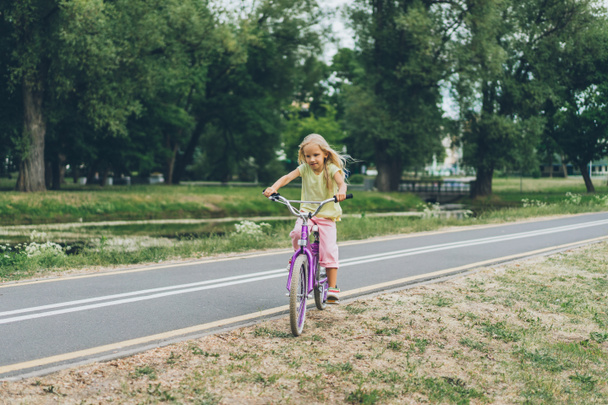 маленька дитина їде на велосипеді по дорозі в парку в літній день
 - Фото, зображення