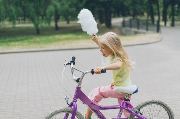 side view of kid with cotton candy on bicycle in park - Foto, Imagen