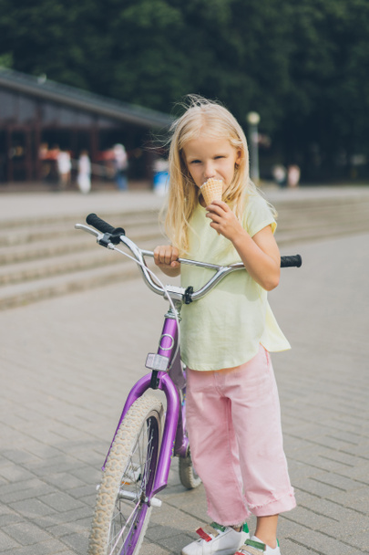adorable little kid with ice cream and bicycle standing on city street - 写真・画像